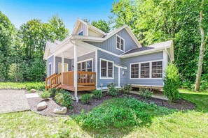 A two-story house with a covered porch, a landscaped garden, and a wooded backdrop.