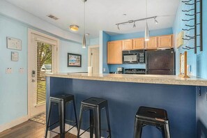 Una cocina con pared azul, armarios de madera, refrigerador de acero inoxidable y una zona de bar con taburetes.