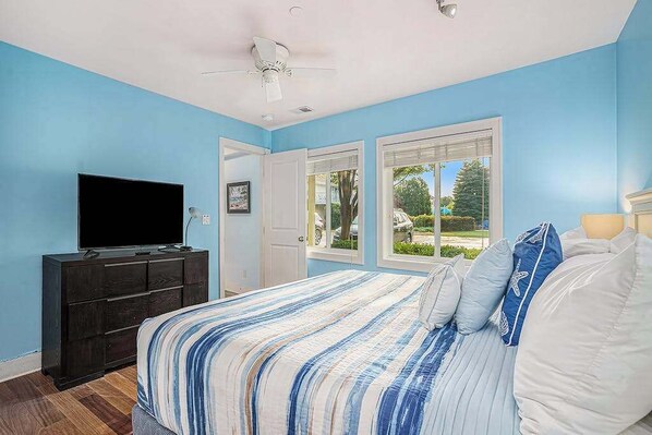 Un dormitorio con cama, televisor sobre una cómoda y vistas al exterior a través de una ventana.