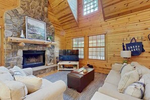 Een gezellig cabin interieur met een stenen open haard, een televisie en een groot raam.
