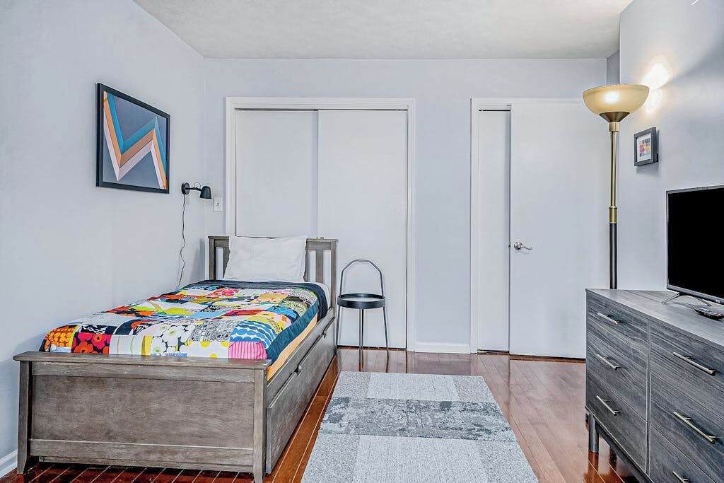 A bedroom with a bed, a dresser, a chair, a lamp, and a television.