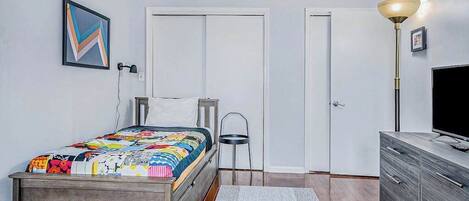 A bedroom with a bed, a dresser, a chair, a lamp, and a television.