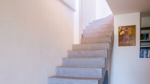 A concrete staircase leading to a second floor, with a bookshelf and framed picture on the wall. - Le Pioulier – Villa in Vence with an open view (Vence)