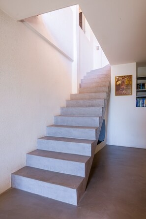 A concrete staircase leading to a second floor, with a bookshelf and framed picture on the wall. - Le Pioulier – Villa in Vence with an open view (Vence)