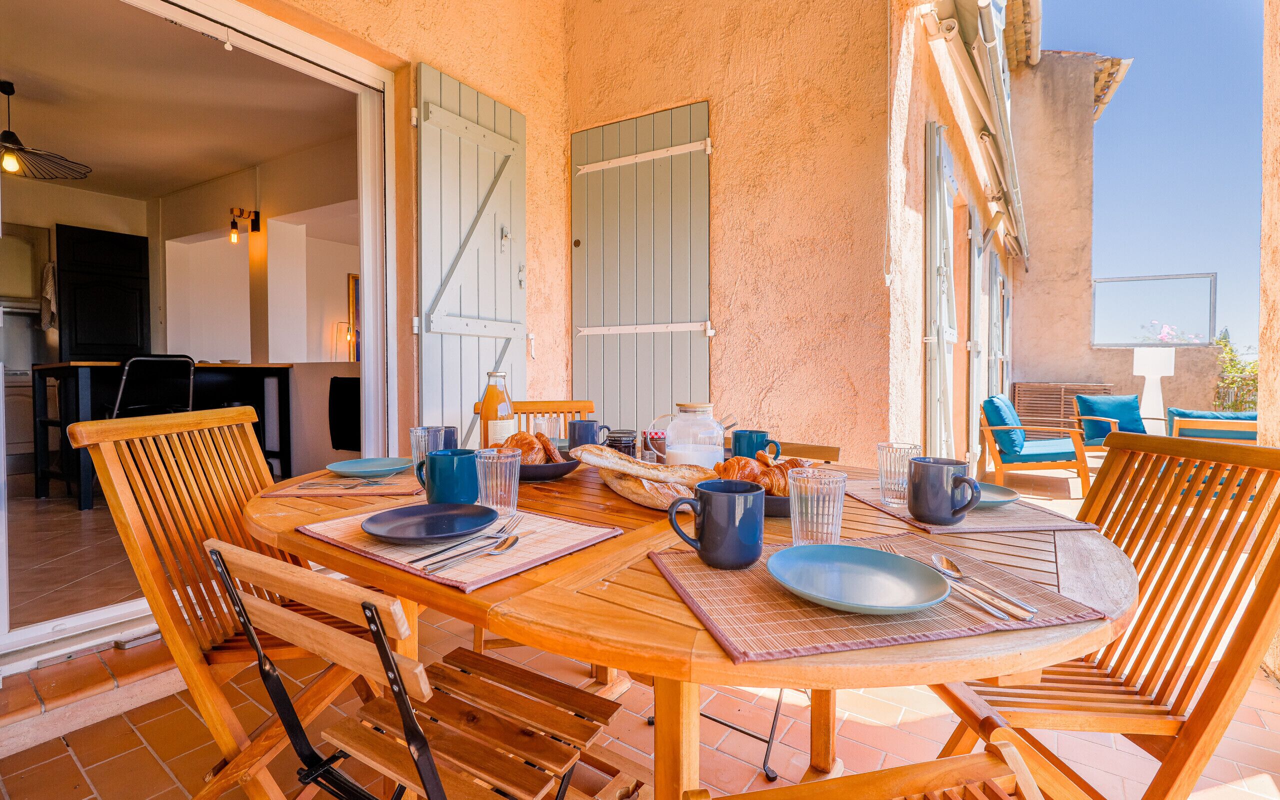 A wooden table set for breakfast with croissants, a bottle of orange juice, and a pitcher of milk.