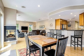 A modern kitchen with a central island, dining area with chairs, and a fireplace. - Riverfront Home w/Private Deck/River Views/Free WiFi - Near Restaurants/Marina (Saugatuck)