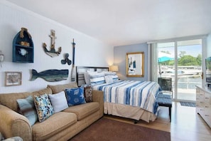 A bedroom with a bed, a sofa, a window with a view of boats, and wall decorations.