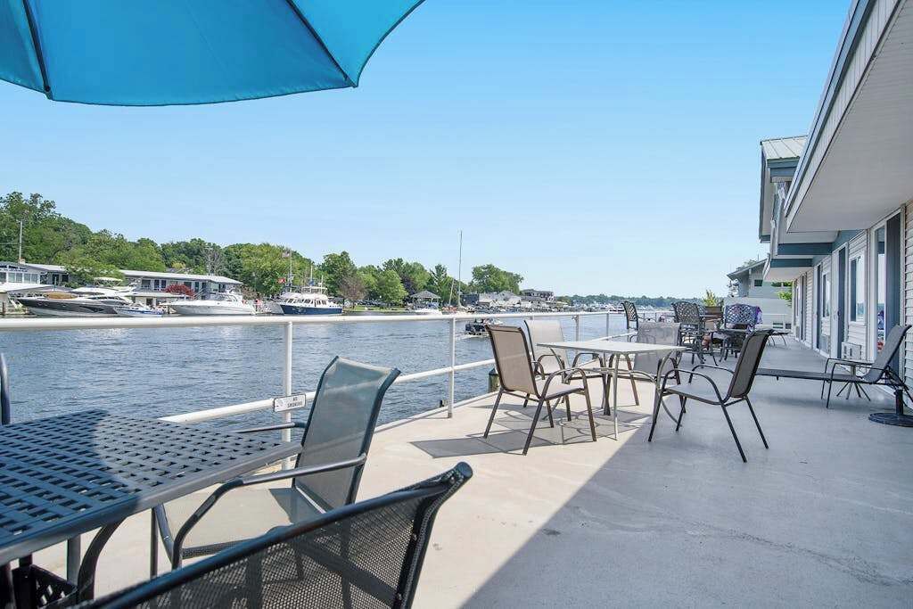 A waterfront patio with tables and chairs, overlooking a marina with boats.