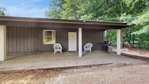 A small building with a porch, two white plastic chairs, a door, and a grill. - Peaceful wooded escape w/ kitchenette, gas grill, WIFI, lakes & trails nearby (Covert)