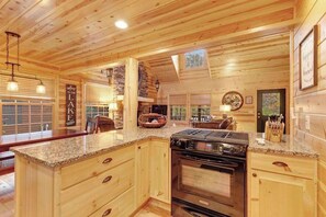 A wooden cabin interior with a kitchen featuring granite countertops, a stove, and a dining area with a table and chairs.