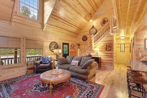 A wooden cabin interior with a living room, dining area, and staircase.