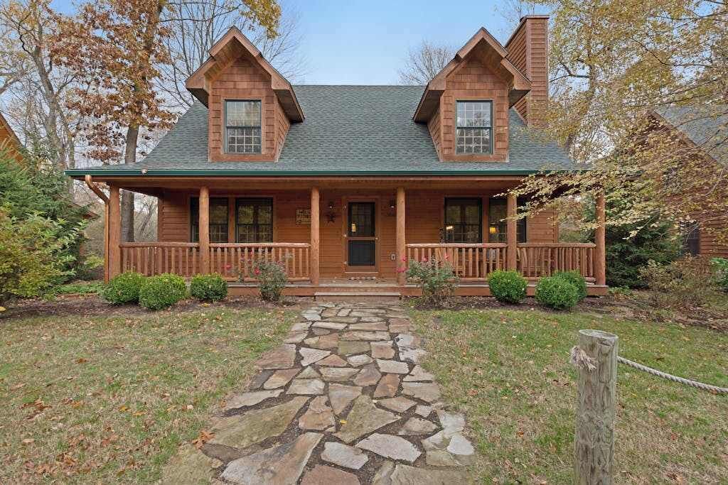 A log cabin with a stone pathway leading to the front door, surrounded by greenery.
