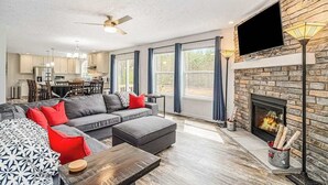 A modern living room with a fireplace, a flat-screen TV, and a dining area in the background. - Four-season retreat with fireplace, firepit, grill, WiFi & central AC (Thompsonville)