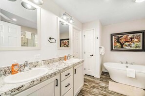 A bathroom with two sinks, a large mirror, a bathtub, and a framed picture on the wall.
