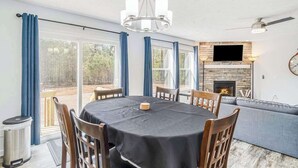 A dining area with a table, chairs, a chandelier, a fireplace, and a television. - Four-season retreat with fireplace, firepit, grill, WiFi & central AC (Thompsonville)