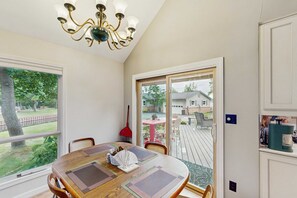 A dining area with a wooden table, chairs, a chandelier, and a view of a backyard through a sliding glass door. - Cottage on the canal to Burt Lake with large patio and space for boat (Indian River)