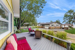 A deck with outdoor furniture, a view of a house, and a grassy area. - Cottage on the canal to Burt Lake with large patio and space for boat (Indian River)