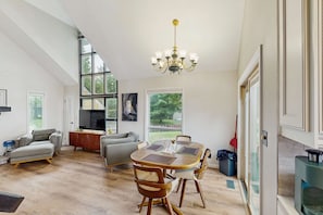 A spacious living area with a high ceiling, a chandelier, a dining table with chairs, a sofa, and a television. - Cottage on the canal to Burt Lake with large patio and space for boat (Indian River)