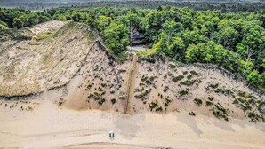 Une propriété située sur la côte, avec une plage de sable, un escalier en bois menant à une maison, et une végétation luxuriante en arrière-plan.
