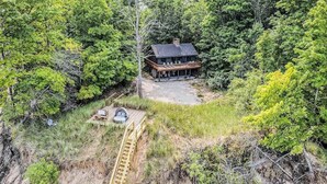 Une cabane entourée d’une forêt dense, dotée d’une terrasse en bois et d’une échelle menant à l’entrée.