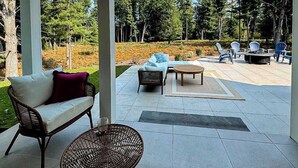 An outdoor patio area with a sofa, wicker chair, and a round table. - Brand New Luxurious Home, w/ Fire pit, Gas Grill, near Lakes & Trails! (Glen Arbor)