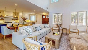 A spacious living area with a sofa, chairs, a coffee table, and a kitchen in the background. - Brand New Luxurious Home, w/ Fire pit, Gas Grill, near Lakes & Trails! (Glen Arbor)
