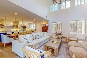 A spacious living area with a sofa, chairs, a coffee table, and a kitchen in the background. - Brand New Luxurious Home, w/ Fire pit, Gas Grill, near Lakes & Trails! (Glen Arbor)