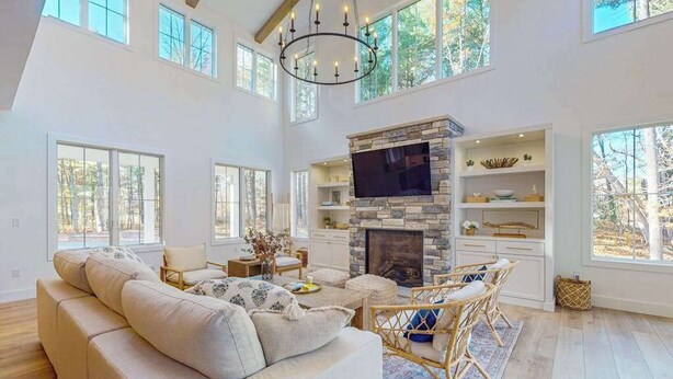 A spacious living room with a stone fireplace, large windows, and a high ceiling. - Brand New Luxurious Home, w/ Fire pit, Gas Grill, near Lakes & Trails! (Glen Arbor)