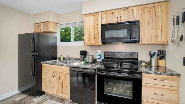 A modern kitchen with wooden cabinets, a black refrigerator, a dishwasher, a stove, and a microwave. - Private dog-friendly hideaway w/  firepit - close to Crystal Mountain (Thompsonville)
