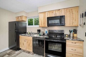 Una cocina moderna con armarios de madera, un refrigerador negro, lavavajillas, estufa y microondas.