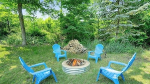A circular fire pit with four blue chairs around it, set in a grassy area with trees in the background. - Private dog-friendly hideaway w/  firepit - close to Crystal Mountain (Thompsonville)