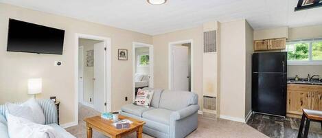 A living room with a sofa, a coffee table, a TV, and a kitchen area with a refrigerator and cabinets.