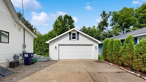 Une maison de plain-pied avec un garage, une allée et un petit jardin bordé d’une haie.