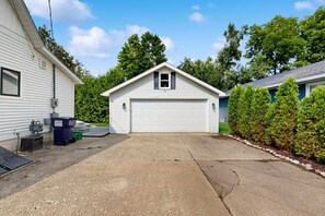 A single-story house with a garage, a driveway, and a small yard with a hedge. - Dreamy Coastal Cottage W/ Free WiFi, Full Kitchen, & Large Deck - Walk to Town (Harbor Springs)