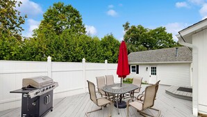 Une terrasse avec un barbecue, une table entourée de chaises et un parasol rouge.