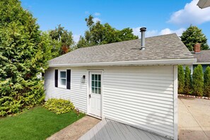 A small, single-story house with a white exterior, a front door, and a chimney. - Dreamy Coastal Cottage W/ Free Wi-Fi, Full Kitchen, & Large Deck - Walk to Town (Harbor Springs)