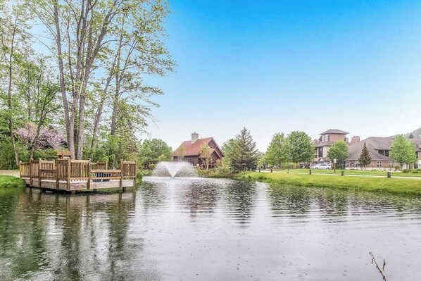 A tranquil pond with a wooden deck and a fountain, surrounded by residential buildings.