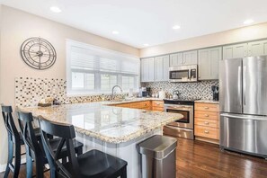 A modern kitchen with a central island, stainless steel appliances, and a clock on the wall.