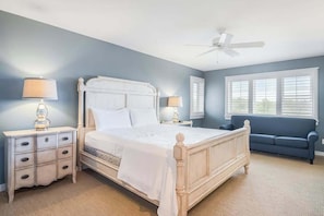 A bedroom with a bed, nightstands, a blue couch, and a ceiling fan.
