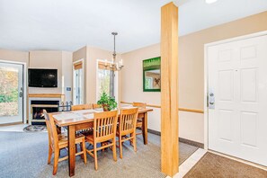 Un comedor con una mesa y sillas de madera, chimenea, televisor y puerta.