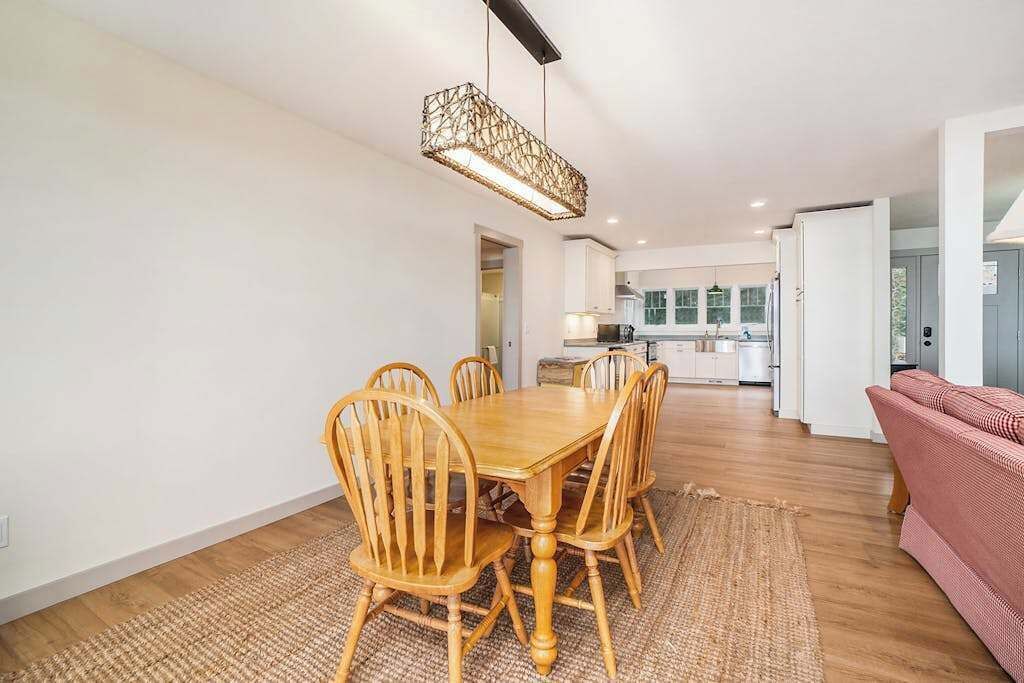 Een eethoek met een houten tafel en stoelen, een geweven vloerkleed en een hanglamp.