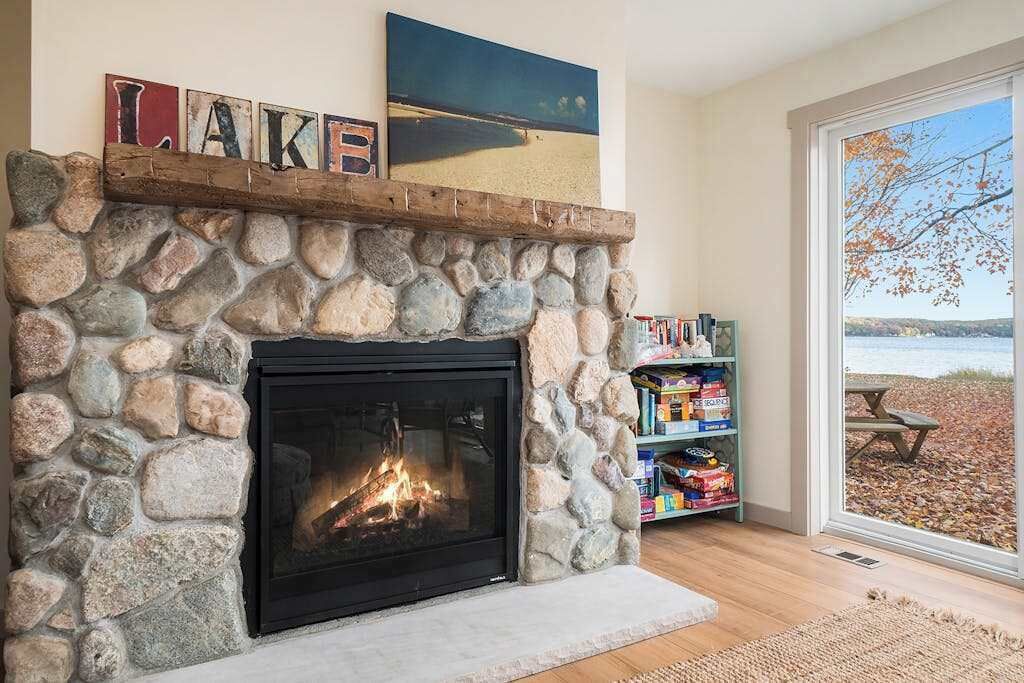 Ein Kamin aus Stein mit Feuer, ein Bücherregal mit Büchern und Blick auf einen Strand durch eine Glastür.