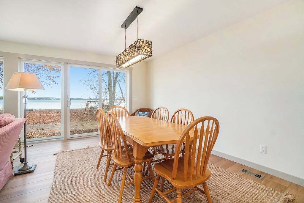 A dining area with a wooden table and chairs, a floor lamp, and a view through large windows.