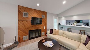 Ein Wohnzimmer mit Kamin, einer Couch, einem Couchtisch und einem an der Wand befestigten Fernseher.