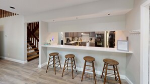 Une cuisine moderne avec un îlot central, des tabourets de bar et un escalier.