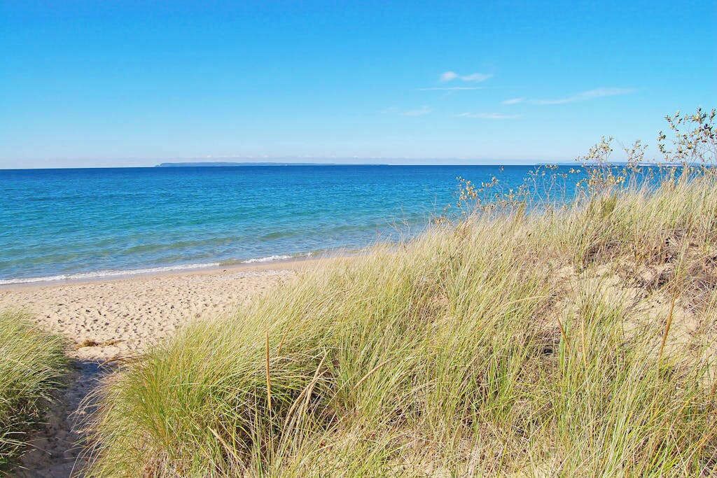 Ein Strand mit klarem Wasser, sandigem Ufer und grasbewachsenen Dünen.