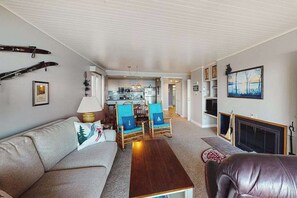 A living room with a sofa, a coffee table, and a fireplace. There is a dining area with chairs and a table.
