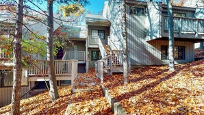 A cabin with a wooden deck, a staircase, and a view of the surrounding forest. - Tasteful Glen Arbor condo with beautiful Lake Michigan views, deck & fireplaces (Glen Arbor)