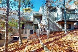A cabin with a wooden deck, a staircase, and a view of the surrounding forest.