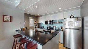 A modern kitchen with a central island, stainless steel appliances, and a clock on the fridge. - Tasteful Glen Arbor condo with beautiful Lake Michigan views, deck & fireplaces (Glen Arbor)